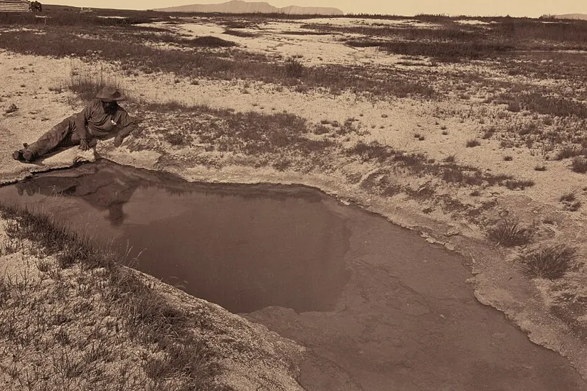 Sepia 1868 photograph of a man reclining beside a hot spring pool in Ruby Valley
